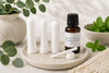 Inhalateur nasal aux huiles essentielles de menthe poivrée, eucalyptus radié, camphre et sapin baumier de La Savonnerie Blanchou, présenté avec son flacon d'huiles essentielles dans un décor naturel.