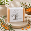 Savon artisanal à l’argousier de La Savonnerie Blanchou présenté dans une ambiance naturelle chaleureuse aux tons orangés inspirés des baies d’argousier
