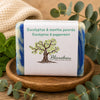 Savon artisanal eucalyptus et menthe poivrée La Savonnerie Blanchou présenté sur plateau de bois avec feuilles d’eucalyptus et menthe