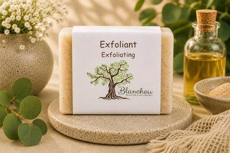 Savon exfoliant artisanal naturel La Savonnerie Blanchou présenté sur une table de bois avec huiles naturelles et feuillage au soleil