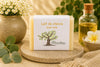 Savon au lait de chèvre artisanal de La Savonnerie Blanchou présenté dans un décor naturel lumineux avec huiles végétales et fleurs