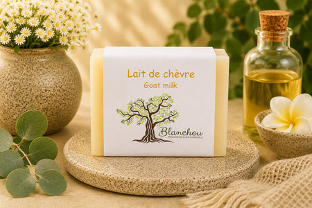 Savon au lait de chèvre artisanal de La Savonnerie Blanchou présenté dans un décor naturel lumineux avec huiles végétales et fleurs