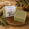 Savon artisanal à l’huile d’olive de La Savonnerie Blanchou présenté avec olives et feuillage dans une ambiance naturelle chaleureuse